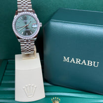 שעון Rolex Datejust 31 עם לוח מנטה ומסגרת יהלומים על מעמד תצוגה, לצד קופסת רולקס